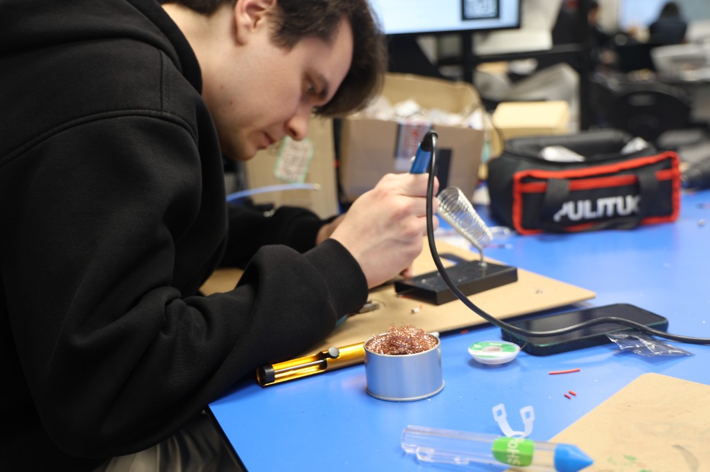 A student soldering a circuit at a workshop bench.